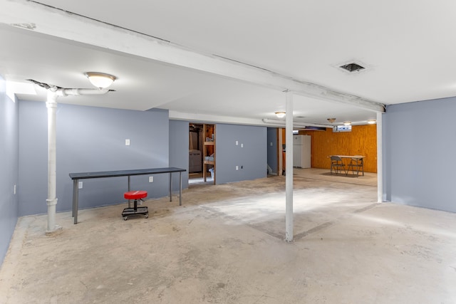 finished basement with visible vents and freestanding refrigerator