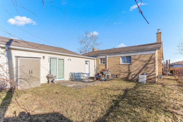 rear view of house featuring a patio, cooling unit, brick siding, a lawn, and a chimney