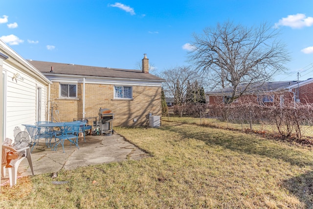 rear view of property featuring brick siding, a yard, a chimney, a patio, and cooling unit