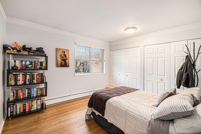 bedroom with baseboard heating, two closets, and wood finished floors