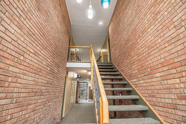 stairway featuring brick wall, carpet flooring, and a high ceiling