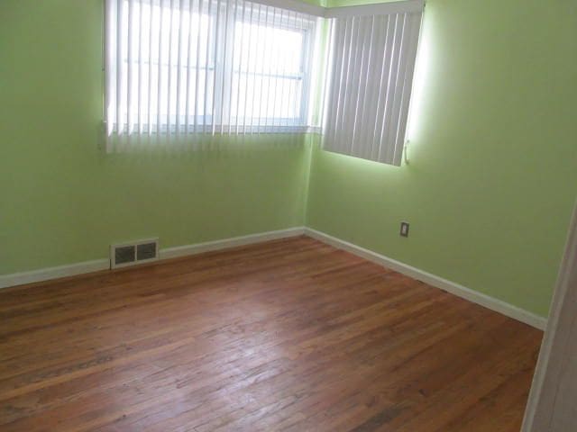 unfurnished room with wood finished floors, visible vents, and baseboards