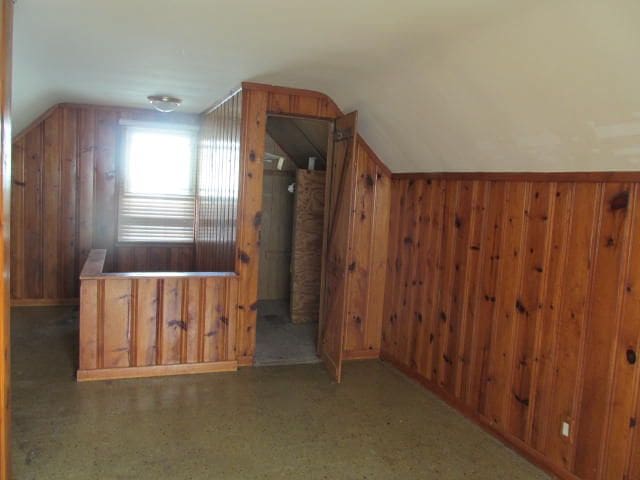 bonus room with vaulted ceiling and wood walls