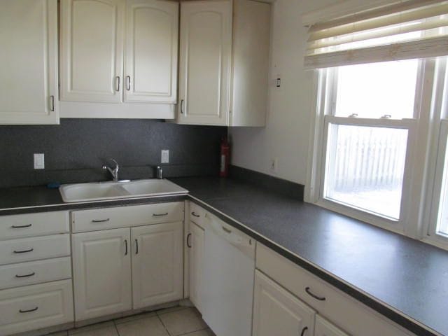 kitchen with light tile patterned floors, a sink, white cabinetry, dishwasher, and dark countertops