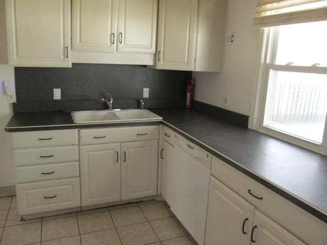 kitchen with dark countertops, white cabinetry, a sink, and dishwasher