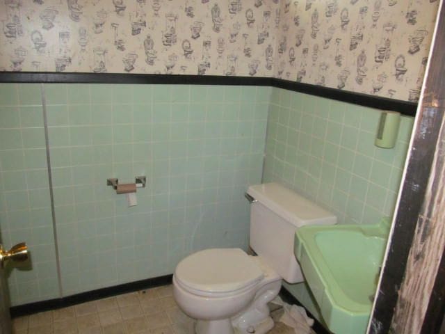 bathroom with toilet, wallpapered walls, and a wainscoted wall