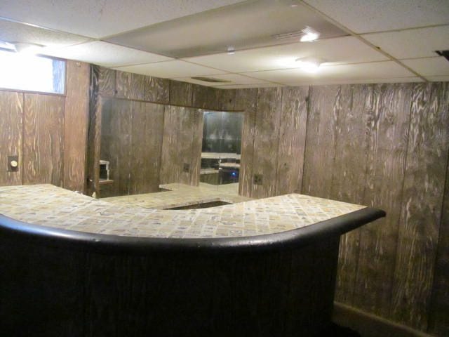 bar with a bar, wooden walls, and a drop ceiling