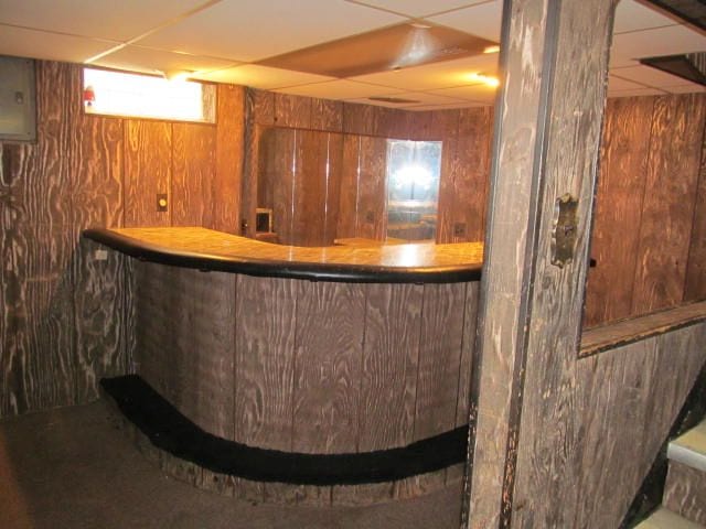 bar with a paneled ceiling, electric panel, wooden walls, and a dry bar