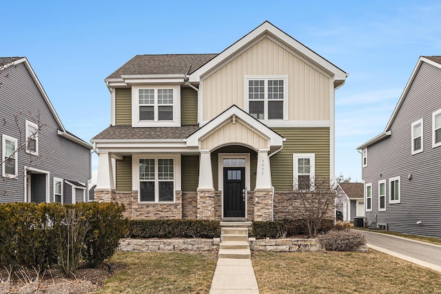 craftsman inspired home featuring stone siding, central AC unit, a front lawn, and a shingled roof