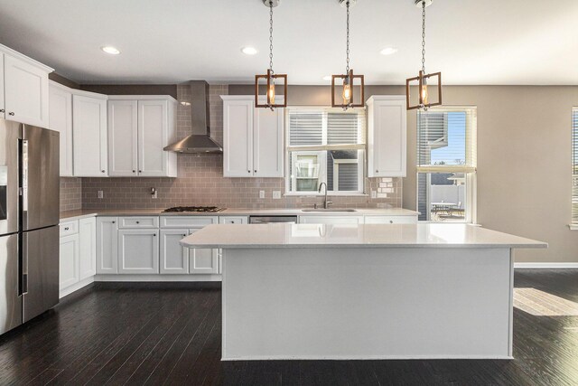 kitchen featuring dark wood-type flooring, a sink, light countertops, wall chimney range hood, and appliances with stainless steel finishes