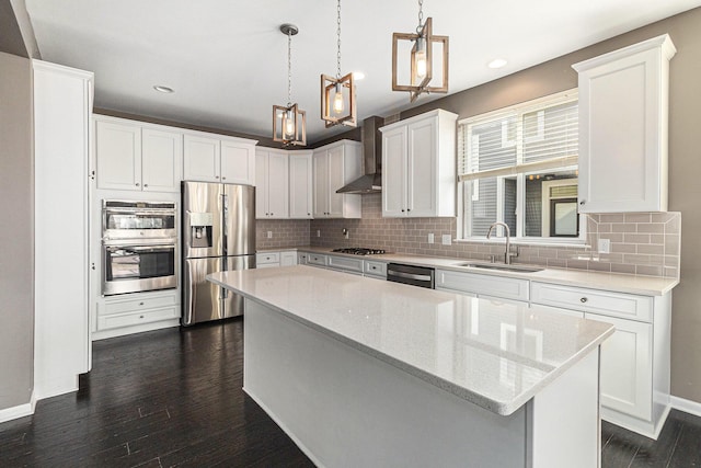 kitchen featuring dark wood-style floors, a center island, appliances with stainless steel finishes, a sink, and wall chimney range hood