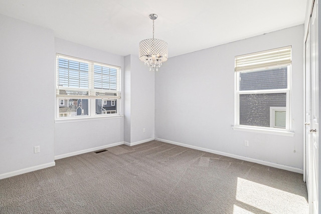 carpeted spare room with baseboards, visible vents, and a chandelier