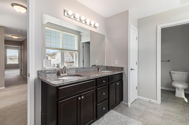 bathroom featuring toilet, double vanity, baseboards, and a sink