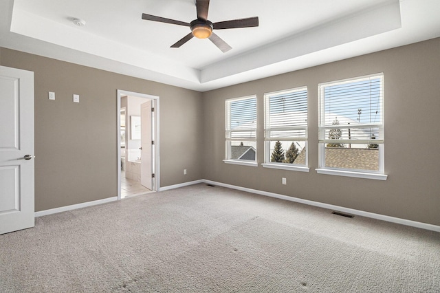 empty room featuring a tray ceiling, light carpet, visible vents, and baseboards