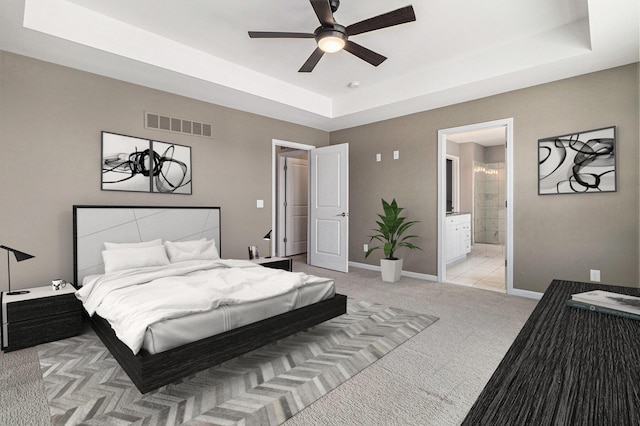 bedroom featuring baseboards, visible vents, connected bathroom, light colored carpet, and a tray ceiling