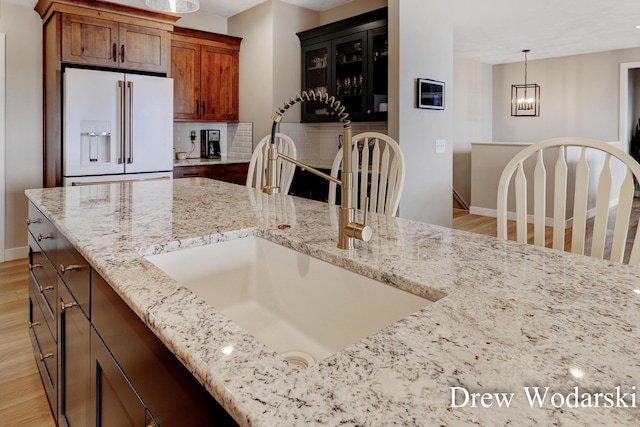 kitchen with high end white fridge, light wood finished floors, a sink, and tasteful backsplash