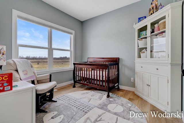 bedroom featuring a nursery area, baseboards, and light wood finished floors