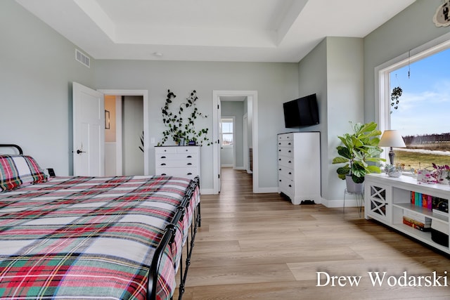 bedroom with light wood-type flooring, baseboards, visible vents, and a raised ceiling