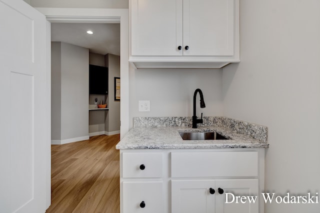 kitchen featuring baseboards, white cabinets, light stone countertops, light wood-type flooring, and a sink