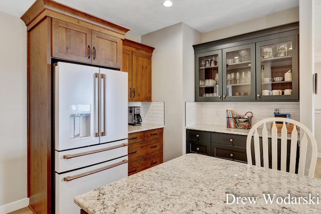 kitchen featuring high end fridge, light stone countertops, glass insert cabinets, and decorative backsplash