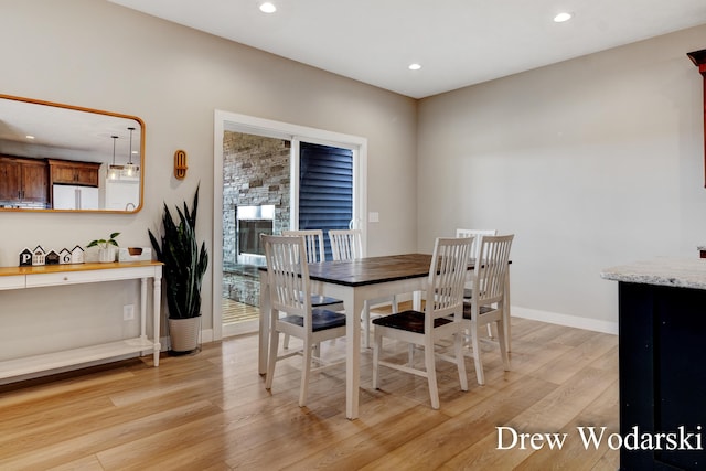 dining room with baseboards, light wood finished floors, a fireplace, and recessed lighting