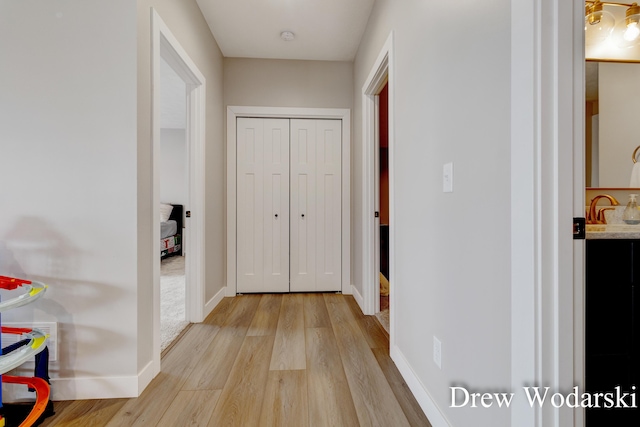 hall featuring light wood-style floors, a sink, and baseboards