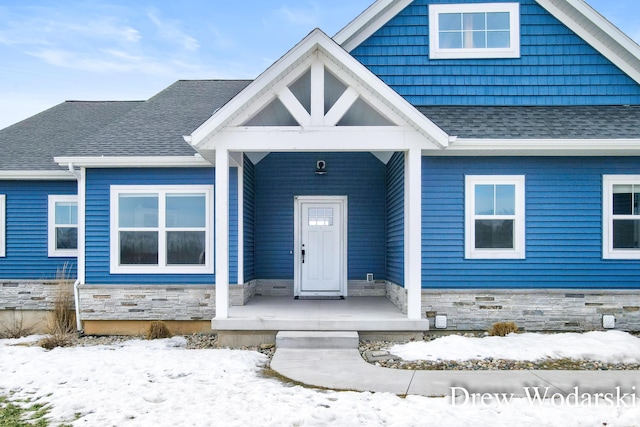 view of front of home featuring stone siding, a porch, and roof with shingles