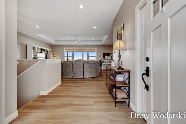 hall with light wood-style floors, a tray ceiling, an upstairs landing, and recessed lighting