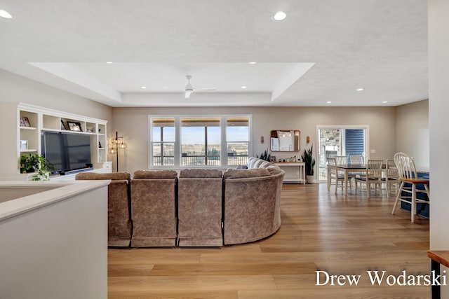 living area with ceiling fan, light wood-type flooring, a raised ceiling, and recessed lighting