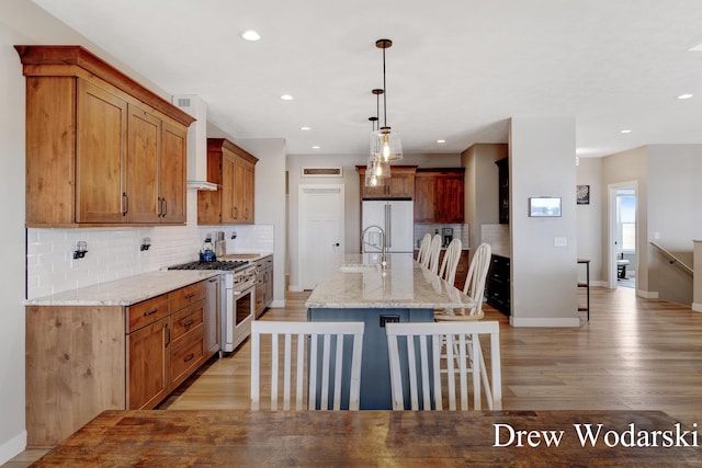 kitchen with premium appliances, a sink, light wood-style floors, wall chimney exhaust hood, and tasteful backsplash