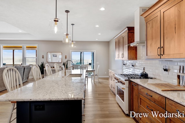 kitchen with tasteful backsplash, a sink, wall chimney range hood, high end stove, and a kitchen bar