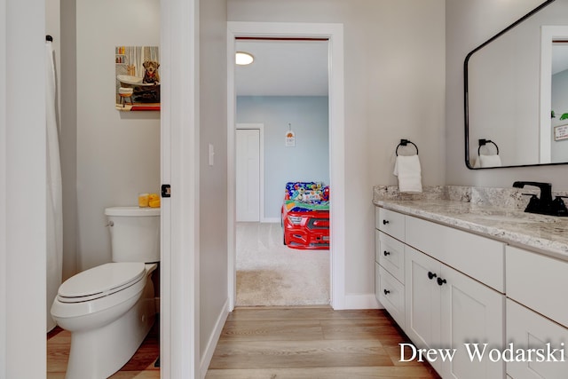 bathroom with toilet, wood finished floors, vanity, and baseboards