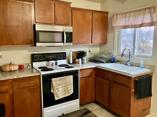 kitchen featuring brown cabinets, range with electric stovetop, light countertops, stainless steel microwave, and a sink