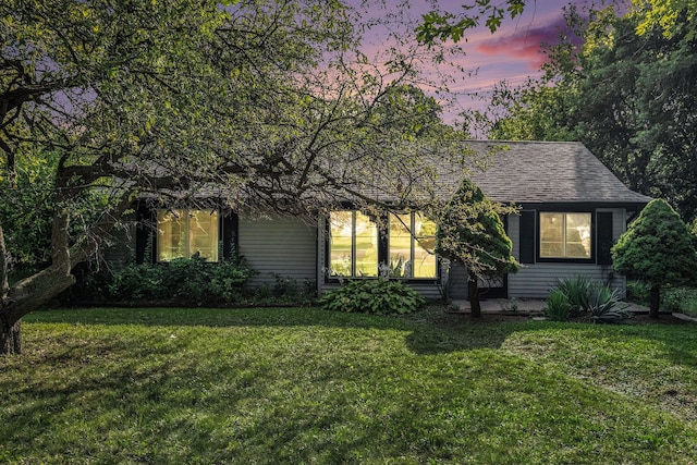 view of property hidden behind natural elements featuring a shingled roof and a lawn