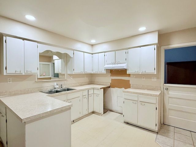 kitchen with recessed lighting, light countertops, a sink, a peninsula, and under cabinet range hood