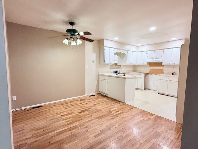 kitchen featuring light wood finished floors, light countertops, white cabinets, under cabinet range hood, and a peninsula