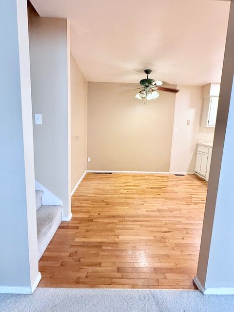 empty room with a ceiling fan, light wood-type flooring, baseboards, and stairs