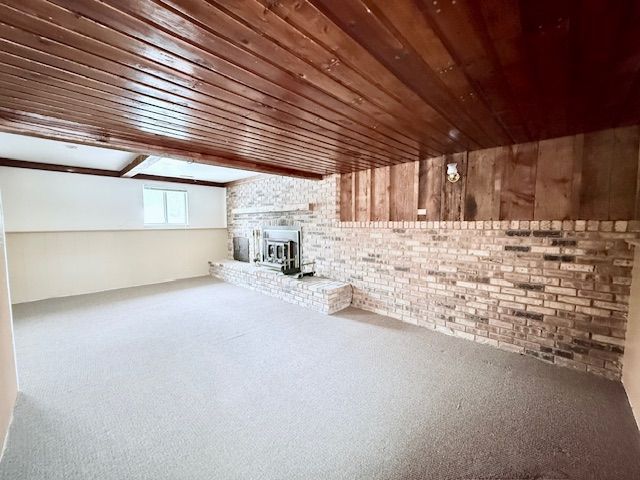 interior space with a wood stove, wooden ceiling, brick wall, and carpet flooring