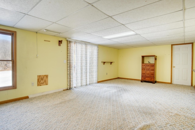 empty room with carpet floors, a drop ceiling, and baseboards