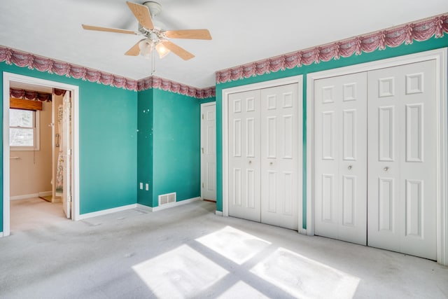 unfurnished bedroom featuring baseboards, visible vents, a ceiling fan, carpet flooring, and two closets