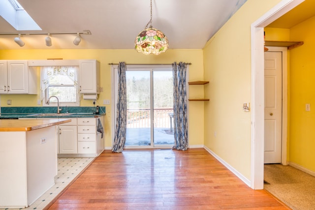 kitchen with light wood-type flooring, a skylight, a sink, and white cabinets