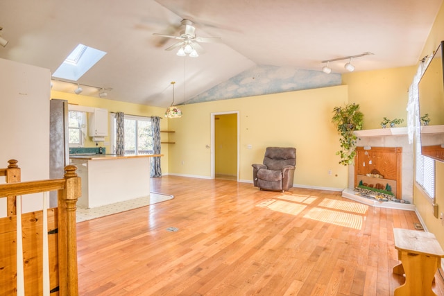 unfurnished living room featuring ceiling fan, vaulted ceiling with skylight, baseboards, and light wood-style floors