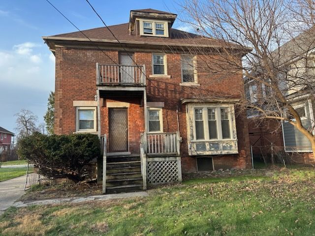 view of front of home with brick siding, a front yard, and a balcony