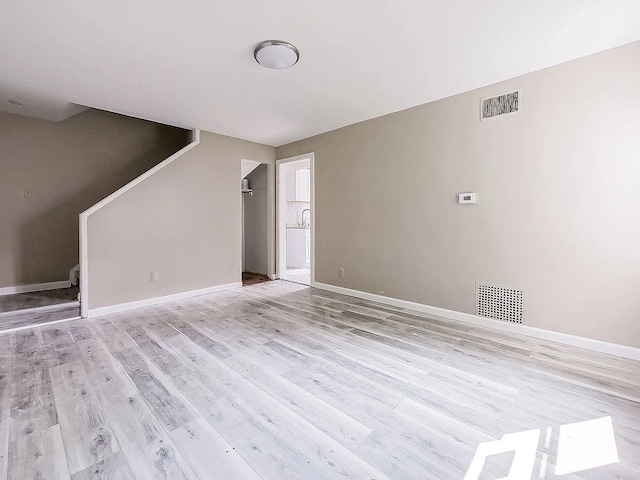 unfurnished living room featuring visible vents, baseboards, light wood-style flooring, and stairs