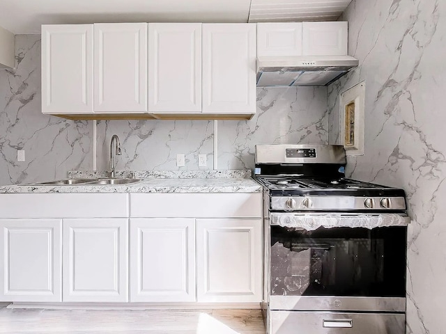 kitchen with under cabinet range hood, a sink, white cabinetry, stainless steel range with gas cooktop, and light stone countertops