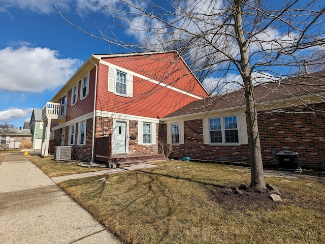 view of front facade featuring brick siding, central AC unit, a front yard, crawl space, and a balcony