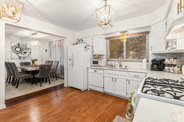 kitchen featuring white appliances, a sink, under cabinet range hood, and an inviting chandelier