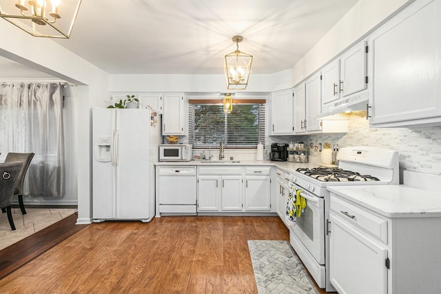 kitchen featuring white appliances, dark wood-style flooring, an inviting chandelier, under cabinet range hood, and a sink