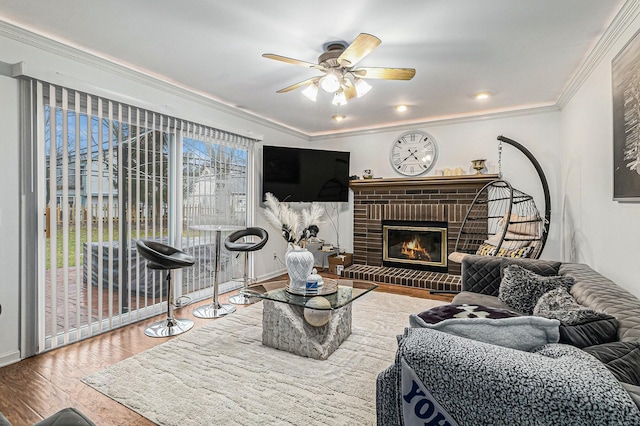 living area with a brick fireplace, a ceiling fan, ornamental molding, and wood finished floors