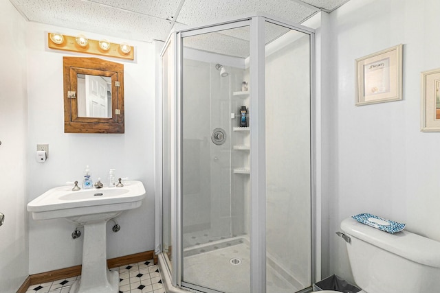 full bathroom featuring toilet, a shower stall, a drop ceiling, baseboards, and tile patterned floors